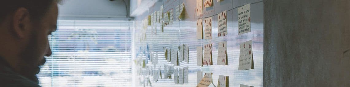 Man looking at white board with sticky notes on it, with a pen in his hand